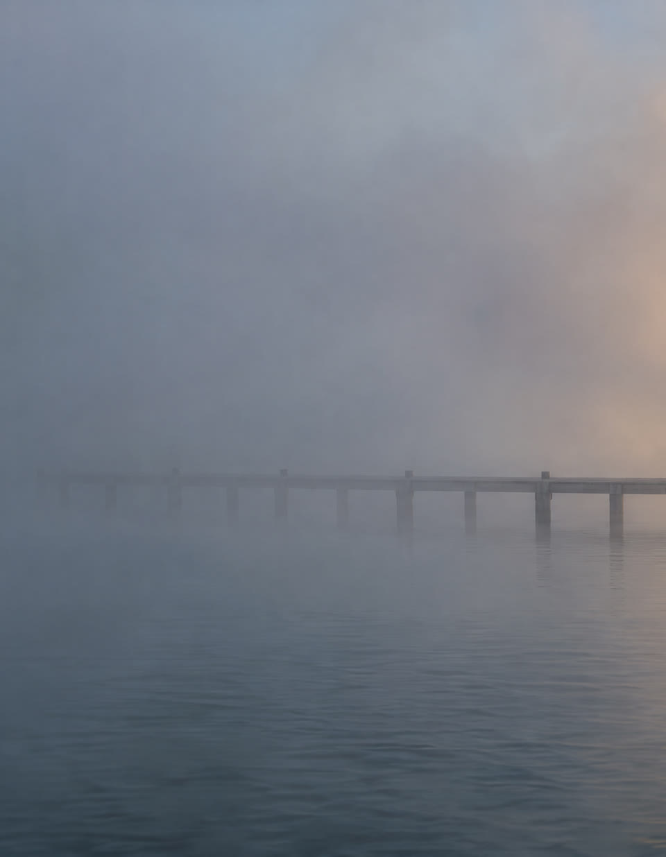 A wooden pier disappearing into dense morning fog.